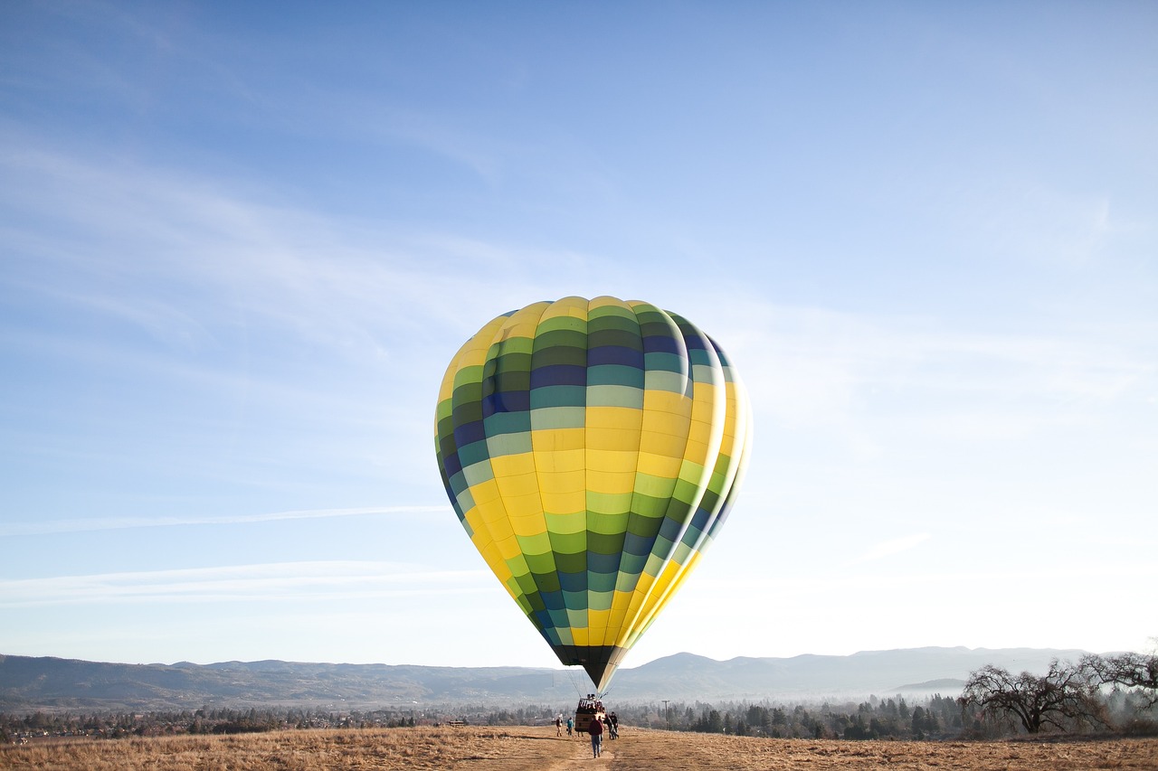 Vor einem klaren Himmel steigt ein gelber Heißluftballon auf, der blau grüne Streifen hat.