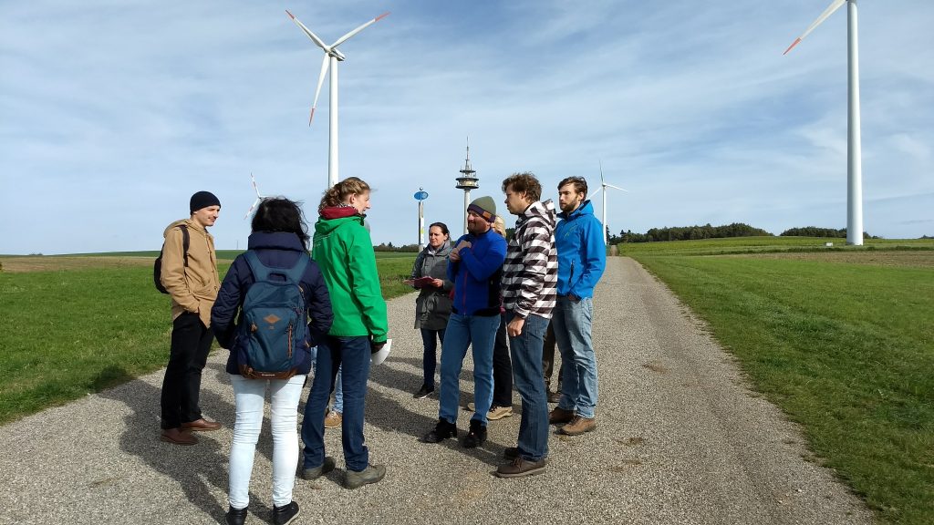 Menschengruppe mit Windrädern im Hintergrund